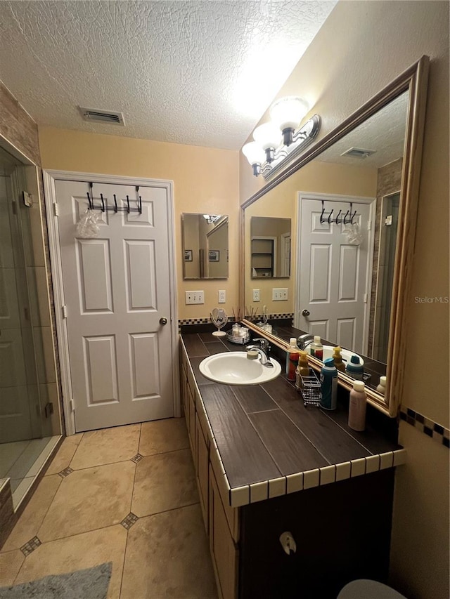 bathroom with tile patterned flooring, a tile shower, vanity, and a textured ceiling