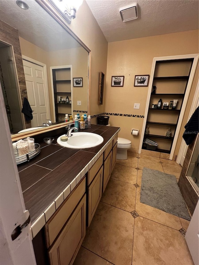 bathroom featuring vanity, tile patterned floors, built in shelves, toilet, and a textured ceiling