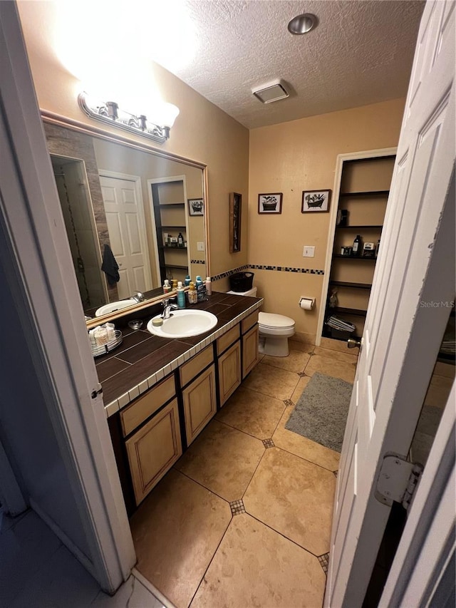 bathroom with tile patterned floors, vanity, a textured ceiling, and toilet