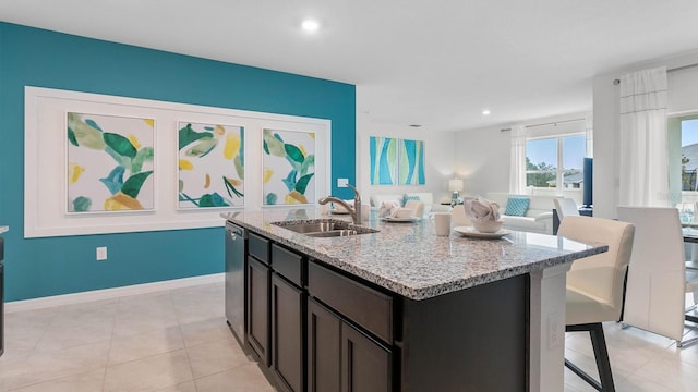 kitchen featuring dishwasher, light stone countertops, sink, and an island with sink