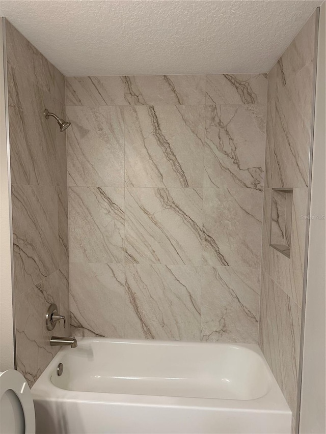 bathroom with tiled shower / bath, toilet, and a textured ceiling