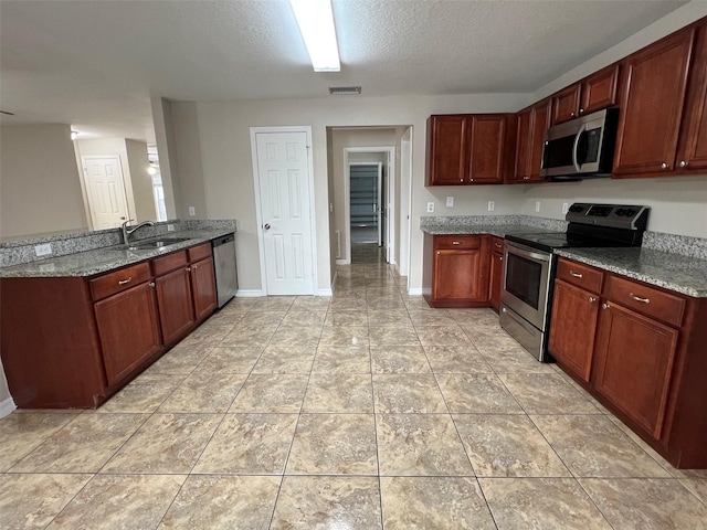 kitchen with kitchen peninsula, a textured ceiling, stainless steel appliances, sink, and dark stone countertops