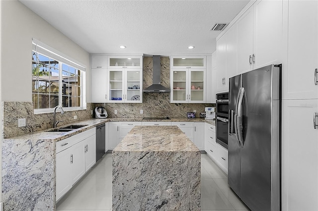 kitchen featuring sink, wall chimney exhaust hood, stainless steel appliances, light stone counters, and white cabinets