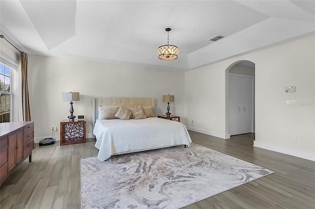 bedroom with wood-type flooring, a raised ceiling, and a notable chandelier