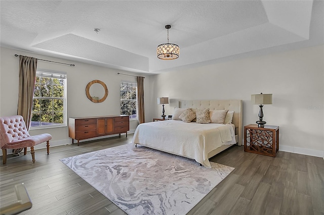 bedroom featuring hardwood / wood-style flooring, a notable chandelier, and a raised ceiling