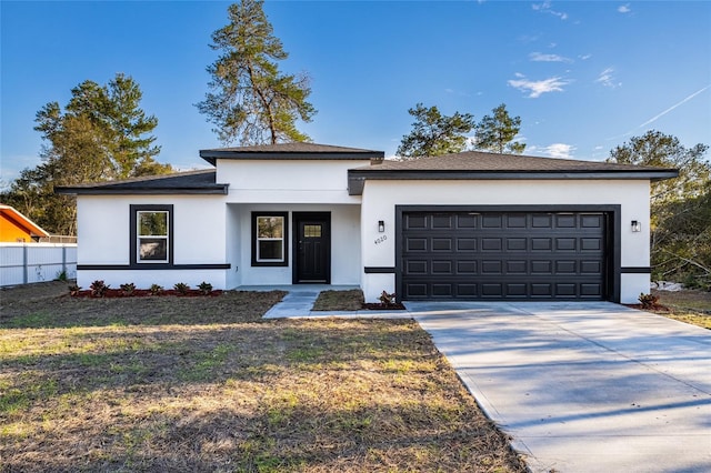 prairie-style house with a garage, fence, driveway, stucco siding, and a front yard