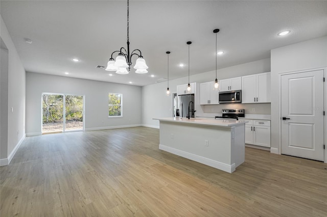 kitchen with light wood-style flooring, white cabinetry, light countertops, appliances with stainless steel finishes, and a center island with sink