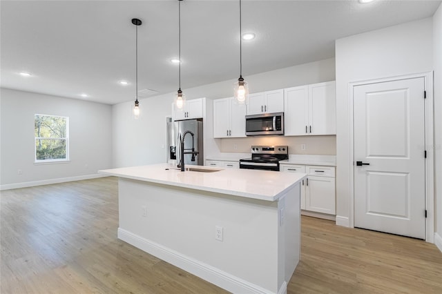 kitchen with light wood finished floors, white cabinets, appliances with stainless steel finishes, a kitchen island with sink, and a sink