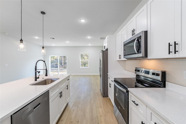 kitchen with appliances with stainless steel finishes, white cabinetry, a sink, and hanging light fixtures