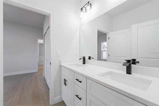 bathroom featuring double vanity, a sink, baseboards, and wood finished floors