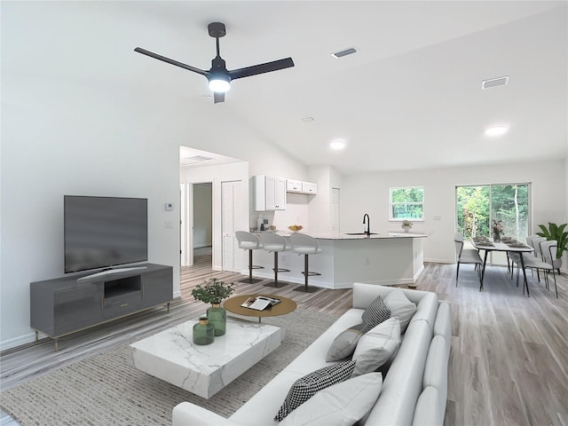 living room featuring light hardwood / wood-style floors, ceiling fan, high vaulted ceiling, and sink