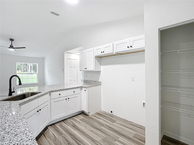 kitchen with lofted ceiling, white cabinets, light stone countertops, and sink