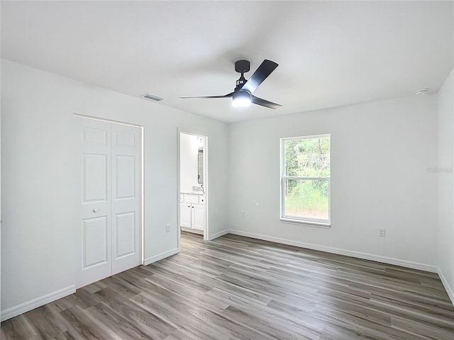 unfurnished bedroom with ceiling fan, a closet, ensuite bath, and hardwood / wood-style flooring