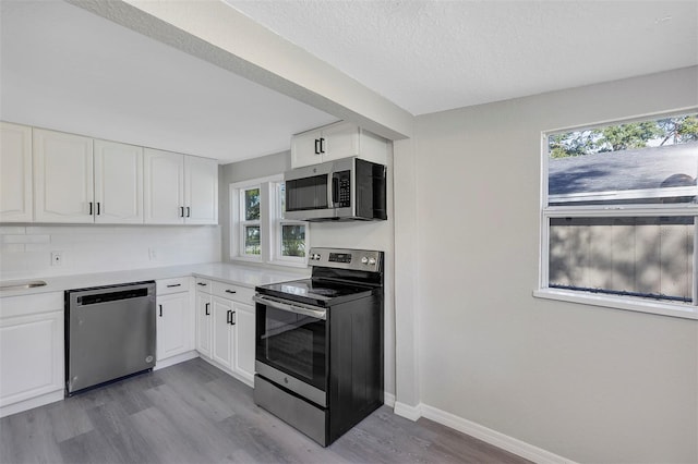 kitchen with tasteful backsplash, white cabinets, stainless steel appliances, and light hardwood / wood-style floors