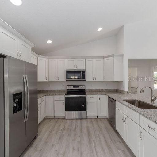 kitchen with light stone countertops, appliances with stainless steel finishes, vaulted ceiling, sink, and white cabinets