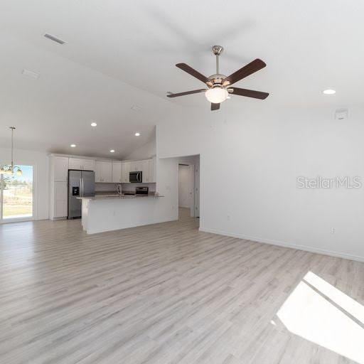 unfurnished living room with ceiling fan, light wood-type flooring, sink, and lofted ceiling