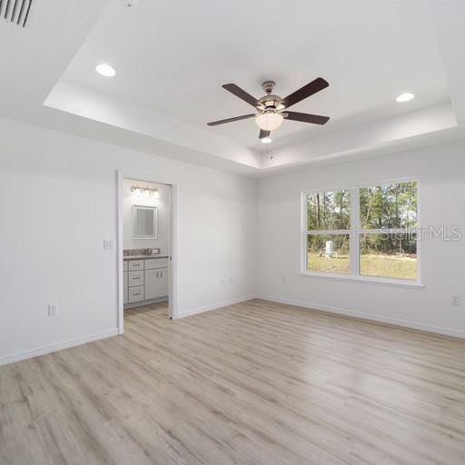 interior space featuring light wood-type flooring, connected bathroom, a raised ceiling, and ceiling fan