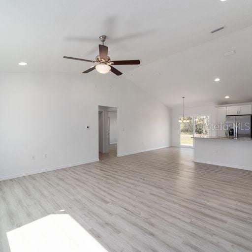 unfurnished living room featuring lofted ceiling, light hardwood / wood-style floors, and ceiling fan with notable chandelier