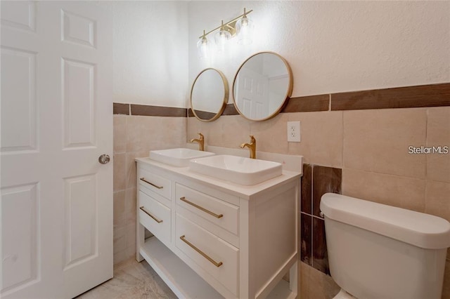 bathroom with double vanity, tile walls, toilet, and a sink