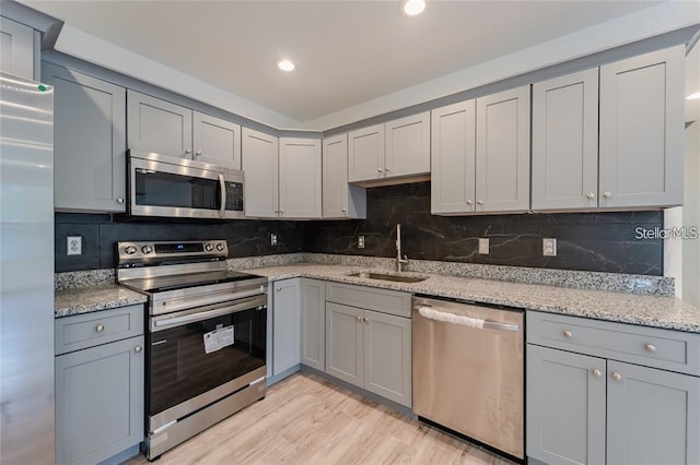 kitchen with stainless steel appliances, a sink, light wood finished floors, and light stone countertops