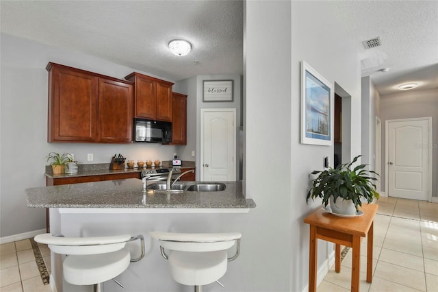 kitchen featuring a breakfast bar, light tile patterned floors, a textured ceiling, and sink