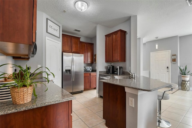 kitchen featuring a kitchen breakfast bar, dark stone counters, stainless steel appliances, sink, and light tile patterned floors