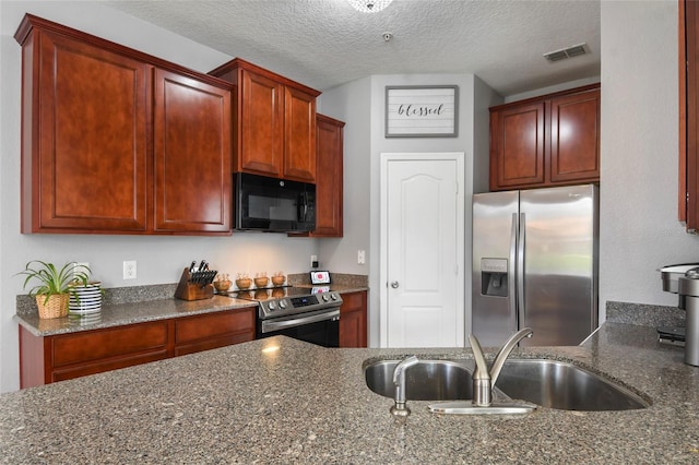 kitchen with a textured ceiling, dark stone countertops, sink, and appliances with stainless steel finishes