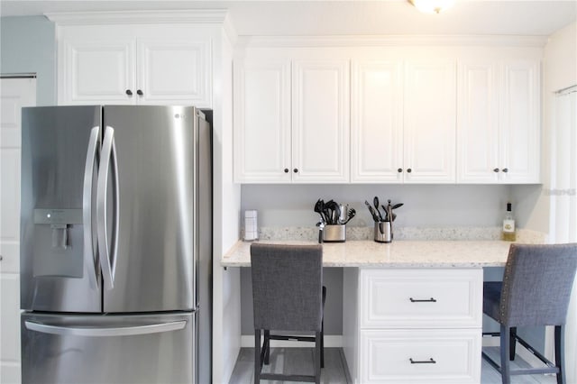 kitchen with a kitchen bar, stainless steel fridge, white cabinets, and light stone counters