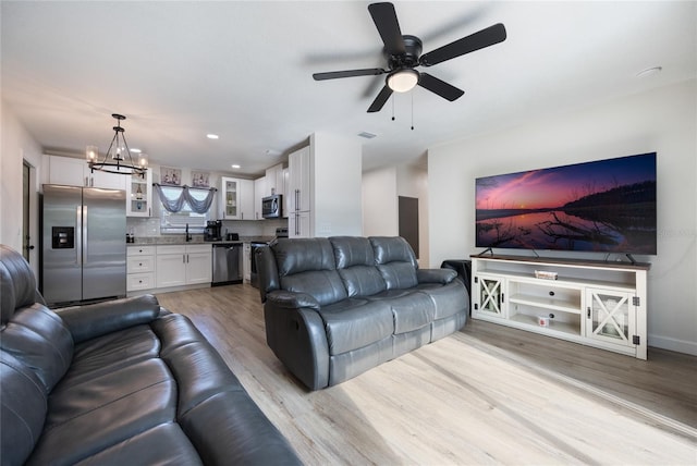 living room featuring ceiling fan with notable chandelier and light hardwood / wood-style flooring