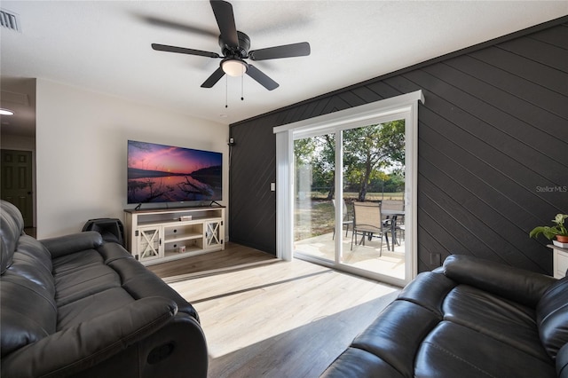 living room featuring light wood-type flooring, ceiling fan, and wood walls