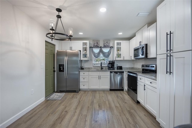 kitchen with light stone countertops, stainless steel appliances, pendant lighting, light hardwood / wood-style flooring, and white cabinetry