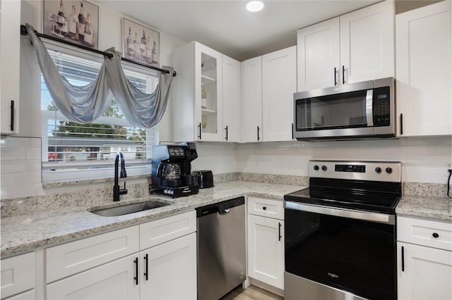 kitchen with white cabinets, stainless steel appliances, light stone counters, and sink