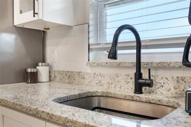 room details with backsplash, white cabinetry, sink, and light stone counters