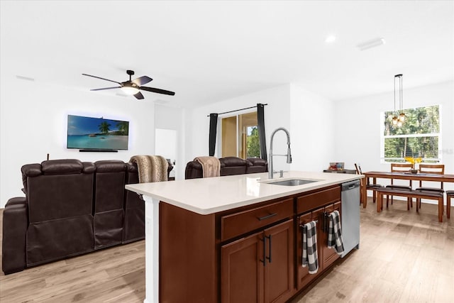 kitchen featuring a kitchen island with sink, sink, light hardwood / wood-style flooring, stainless steel dishwasher, and decorative light fixtures