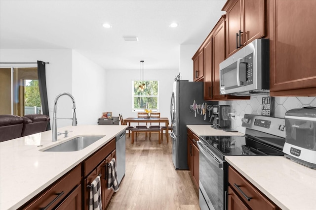 kitchen featuring decorative backsplash, appliances with stainless steel finishes, sink, light hardwood / wood-style floors, and hanging light fixtures