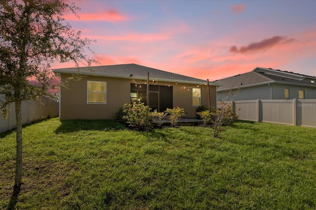 back house at dusk featuring a lawn