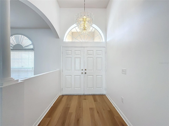 foyer with a chandelier, wood-type flooring, a towering ceiling, and a wealth of natural light