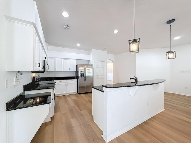 kitchen featuring light wood-type flooring, stainless steel appliances, pendant lighting, white cabinetry, and an island with sink