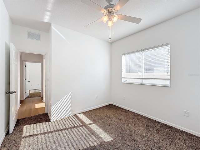 empty room with dark colored carpet, ceiling fan, and a textured ceiling