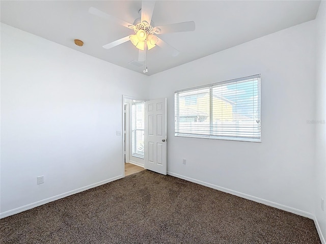 spare room with dark carpet, ceiling fan, and a healthy amount of sunlight