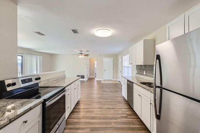 kitchen with stainless steel appliances, white cabinets, hardwood / wood-style flooring, tasteful backsplash, and light stone countertops