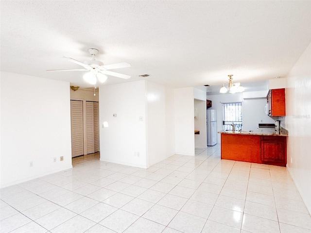 tiled empty room with a textured ceiling and ceiling fan with notable chandelier