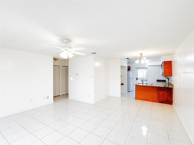 kitchen with ceiling fan with notable chandelier, light tile patterned floors, a textured ceiling, white fridge, and kitchen peninsula