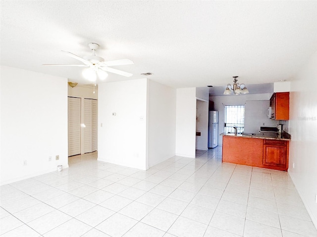 kitchen featuring kitchen peninsula, a textured ceiling, ceiling fan with notable chandelier, light tile patterned floors, and white refrigerator