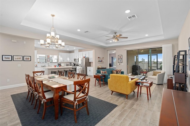 dining area featuring a tray ceiling and ceiling fan with notable chandelier