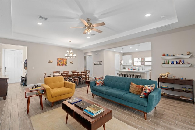 living room featuring ceiling fan with notable chandelier, sink, and a tray ceiling