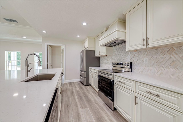 kitchen featuring light stone countertops, sink, light hardwood / wood-style flooring, premium range hood, and appliances with stainless steel finishes