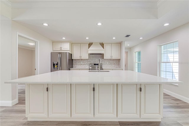 kitchen with appliances with stainless steel finishes, tasteful backsplash, a spacious island, and custom exhaust hood