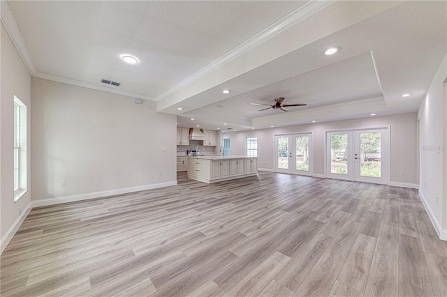 unfurnished living room featuring french doors, a tray ceiling, ceiling fan, crown molding, and light hardwood / wood-style flooring