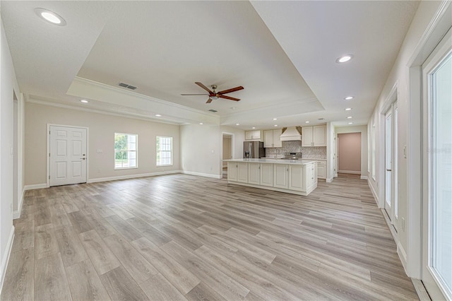 unfurnished living room featuring a raised ceiling, ceiling fan, crown molding, and light hardwood / wood-style floors